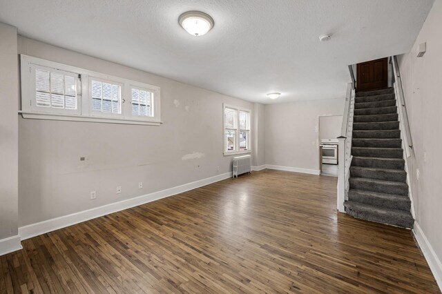 basement with a textured ceiling, wood finished floors, baseboards, radiator heating unit, and stairs
