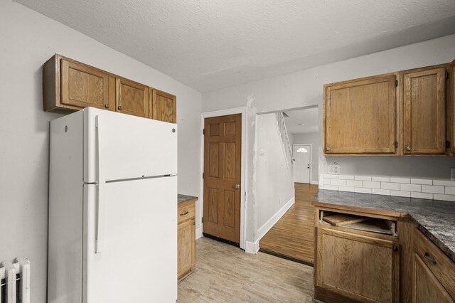 kitchen with dark countertops, light wood-style floors, brown cabinetry, radiator, and freestanding refrigerator