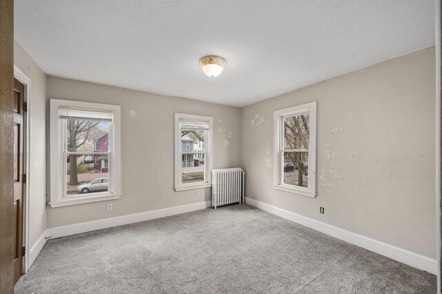 carpeted empty room featuring a textured ceiling, baseboards, a wealth of natural light, and radiator heating unit