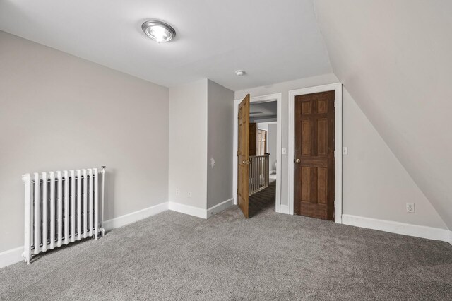 interior space featuring vaulted ceiling, radiator, baseboards, and carpet flooring