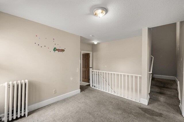 empty room featuring carpet floors, radiator, and baseboards