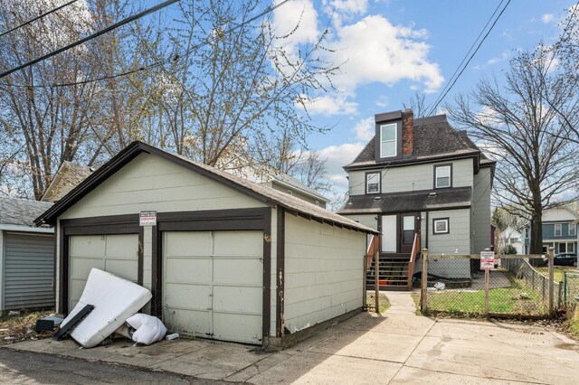 view of front facade with a garage, fence, roof with shingles, entry steps, and an outbuilding