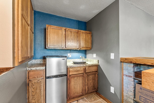 9158 Collins Dr NW, Ramsey, MN 55303 - kitchen with freestanding refrigerator, a textured ceiling, brown cabinetry, light countertops, and a textured wall