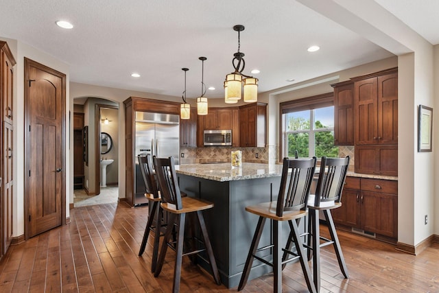 2919 Hilltop Dr, Chaska, MN 55318 - kitchen featuring appliances with stainless steel finishes, arched walkways, hardwood / wood-style floors, a center island, and tasteful backsplash