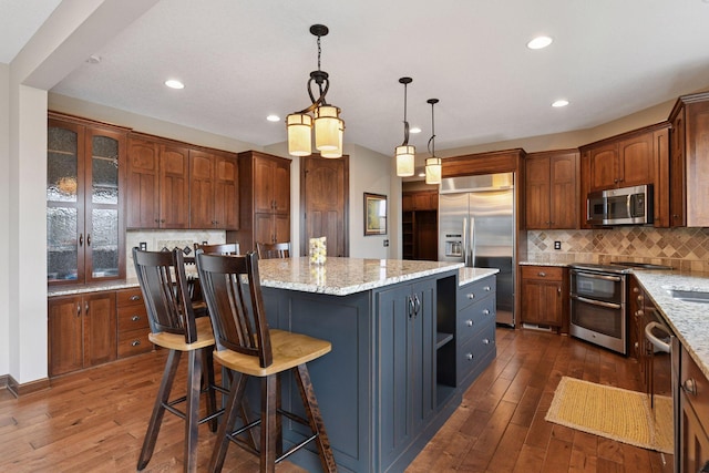 2919 Hilltop Dr, Chaska, MN 55318 - kitchen featuring appliances with stainless steel finishes, a center island, dark wood-type flooring, decorative backsplash, and light stone countertops