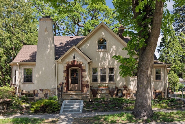 tudor house with a chimney, roof with shingles, stone siding, and stucco siding