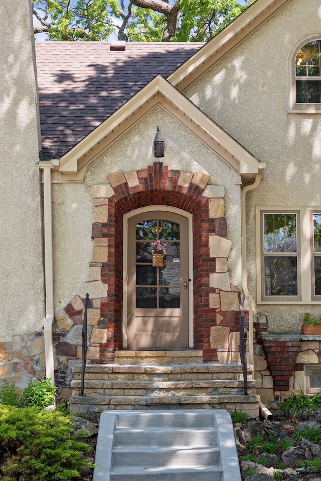 doorway to property with stucco siding, roof with shingles, and brick siding