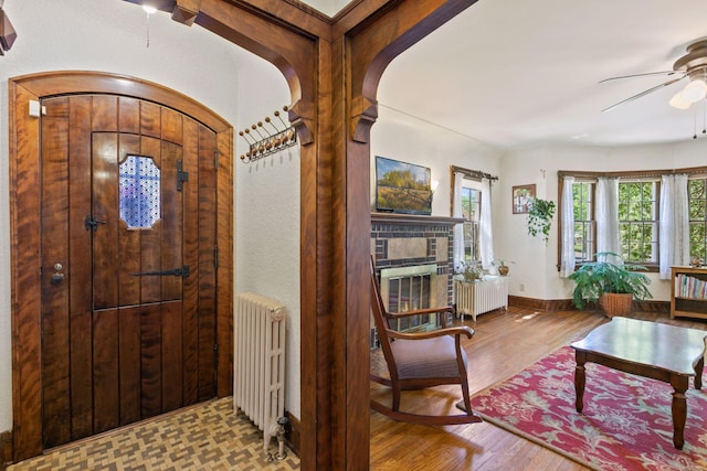 entrance foyer with radiator heating unit, ceiling fan, wood finished floors, and arched walkways