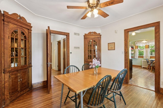 dining area featuring radiator heating unit, wood finished floors, a ceiling fan, and baseboards