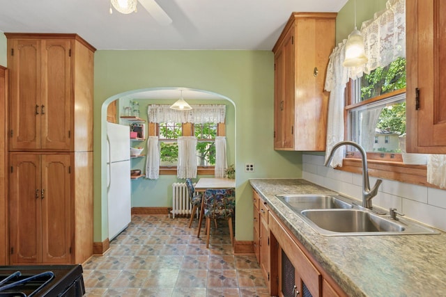 kitchen featuring radiator heating unit, a sink, baseboards, brown cabinetry, and freestanding refrigerator