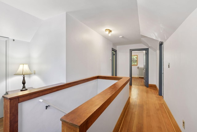 hallway with an upstairs landing, light wood-style flooring, radiator heating unit, baseboards, and lofted ceiling