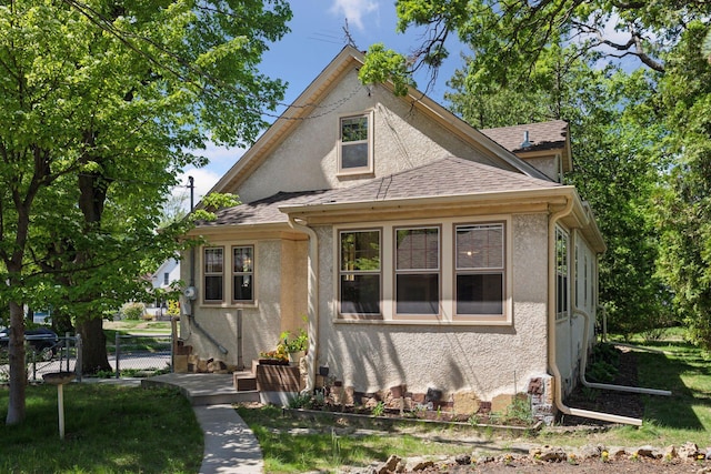 bungalow with a shingled roof, stucco siding, and fence