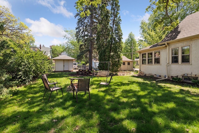 view of green lawn with a storage shed, an outbuilding, and an outdoor fire pit