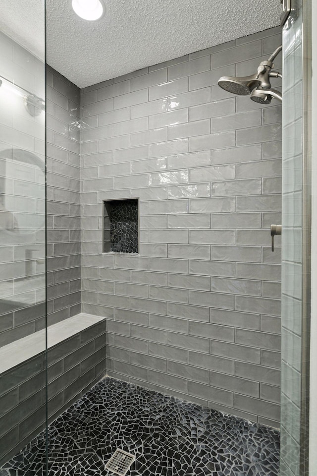 bathroom featuring a textured ceiling, a tile shower, and marble finish floor