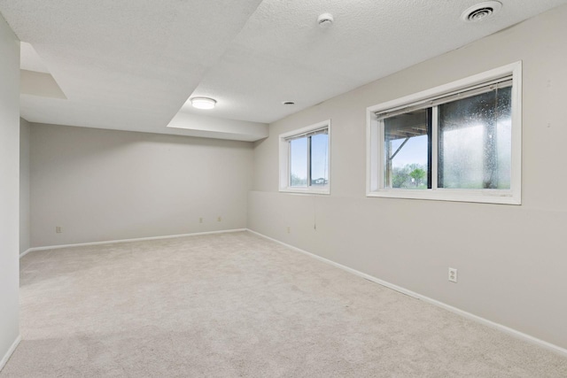 below grade area featuring a textured ceiling, baseboards, visible vents, and carpet
