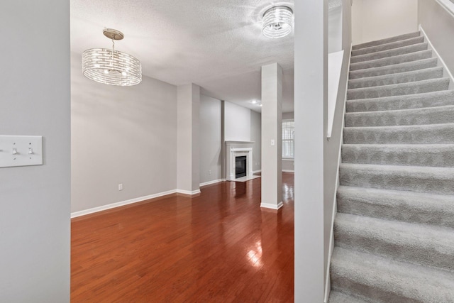 stairs with baseboards, a fireplace with flush hearth, a textured ceiling, and wood finished floors
