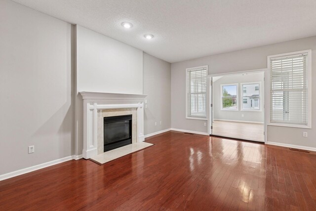unfurnished living room featuring a high end fireplace, baseboards, a textured ceiling, and hardwood / wood-style floors