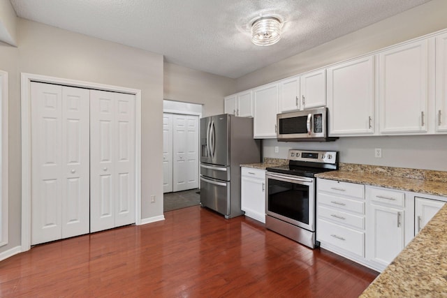 kitchen featuring appliances with stainless steel finishes, white cabinets, light stone countertops, and dark wood-type flooring