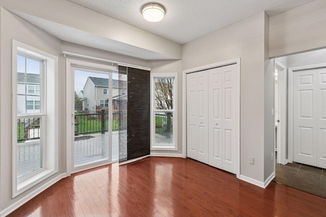 interior space with a textured ceiling, wood finished floors, multiple windows, and access to exterior