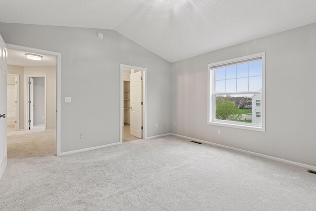 unfurnished bedroom with baseboards, light carpet, lofted ceiling, and visible vents