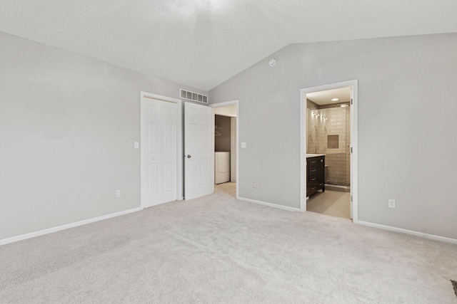 unfurnished bedroom featuring baseboards, light carpet, vaulted ceiling, and washer / clothes dryer