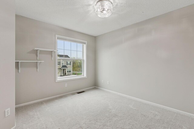 carpeted empty room featuring baseboards, a textured ceiling, and visible vents