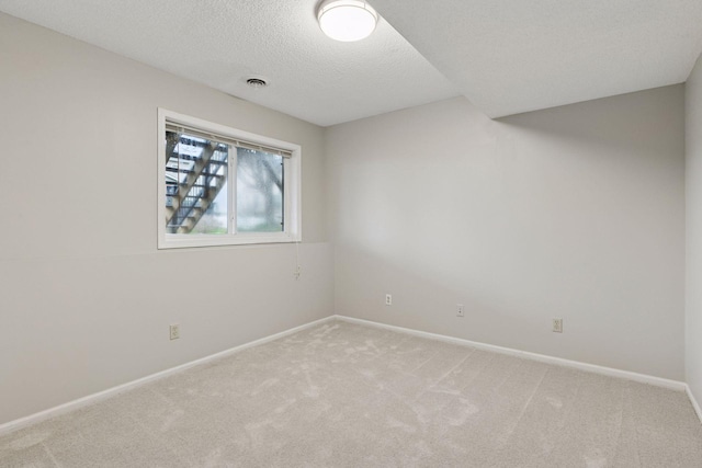 empty room featuring baseboards, light carpet, a textured ceiling, and visible vents