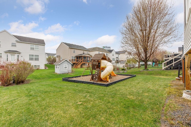 view of playground with a residential view, a storage unit, fence, a lawn, and an outdoor structure