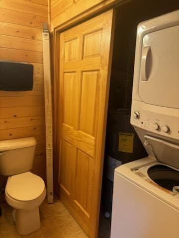 19675 Woody Ln NE, Kelliher, MN 56650 - interior space featuring stacked washer / dryer, wood walls, tile patterned flooring, and toilet