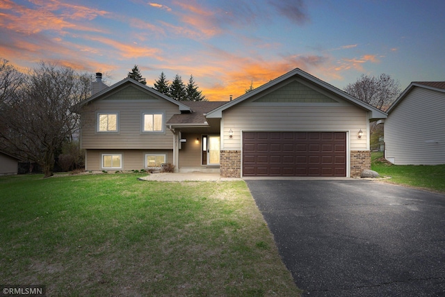 split level home with a chimney, a lawn, driveway, brick siding, and an attached garage