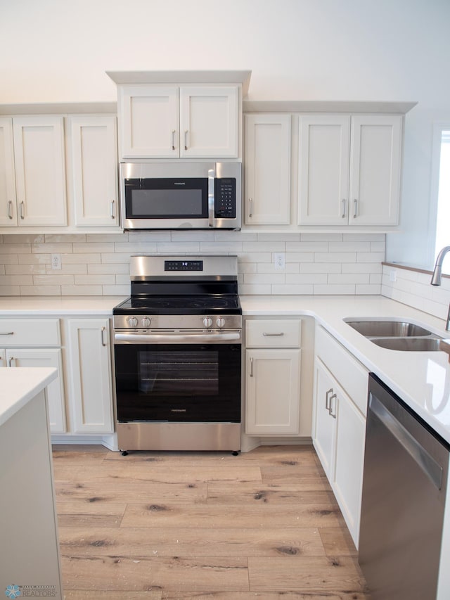 kitchen featuring stainless steel appliances, backsplash, a sink, and white cabinetry
