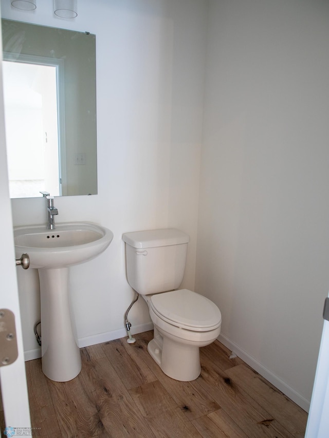bathroom featuring baseboards, wood finished floors, a sink, and toilet