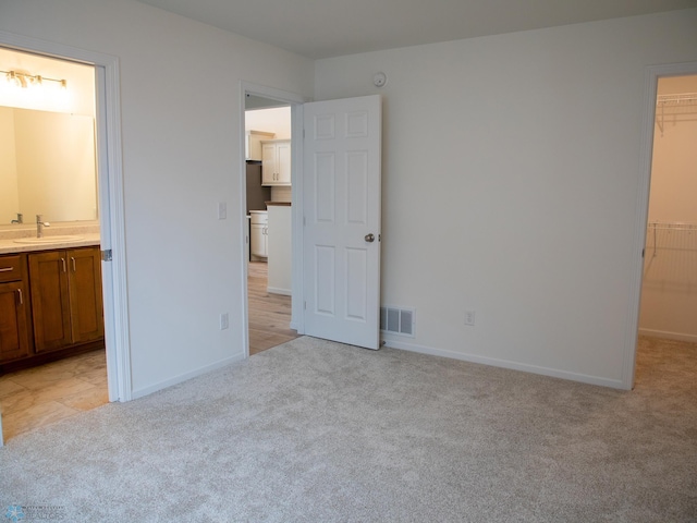 unfurnished bedroom featuring a spacious closet, visible vents, a sink, baseboards, and light colored carpet