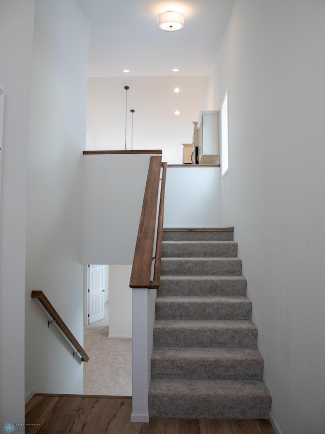 stairs with wood finished floors and recessed lighting
