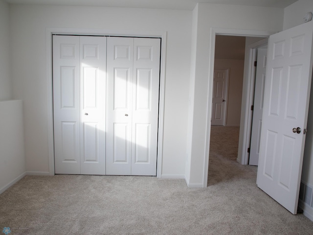unfurnished bedroom with light carpet, baseboards, and a closet