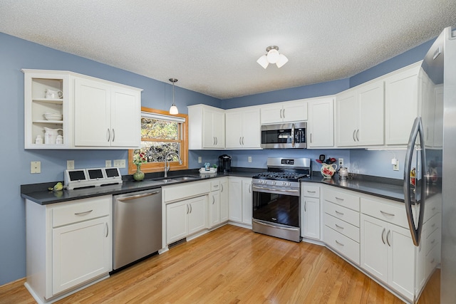 kitchen with dark countertops, a sink, white cabinetry, light wood finished floors, and appliances with stainless steel finishes