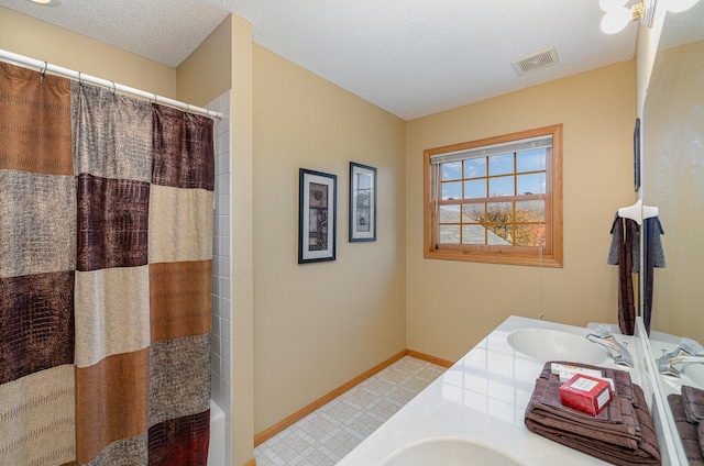 full bath featuring double vanity, visible vents, a sink, baseboards, and a textured ceiling