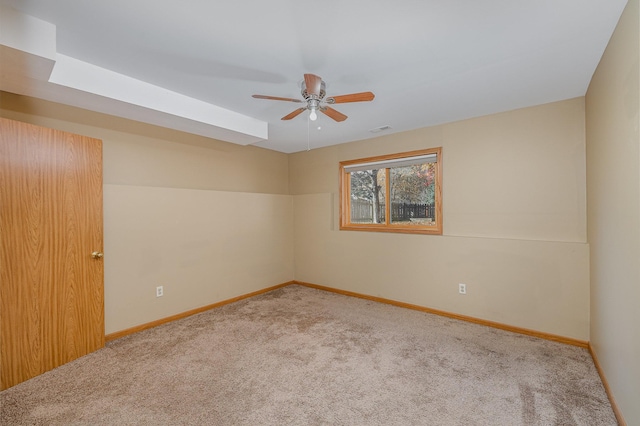 spare room featuring visible vents, a skylight, baseboards, carpet flooring, and ceiling fan