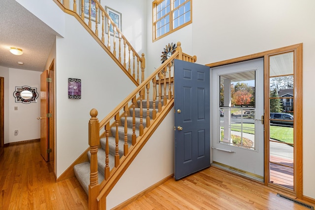 entrance foyer featuring stairway, a towering ceiling, light wood-style flooring, baseboards, and visible vents