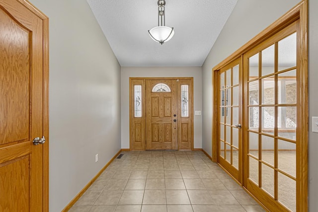 entryway featuring lofted ceiling, a textured ceiling, baseboards, light tile patterned flooring, and french doors