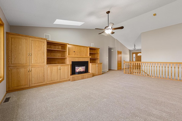 unfurnished living room featuring visible vents, ceiling fan, carpet flooring, and vaulted ceiling with skylight