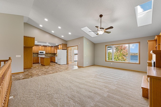 unfurnished living room with baseboards, recessed lighting, light carpet, lofted ceiling with skylight, and a ceiling fan