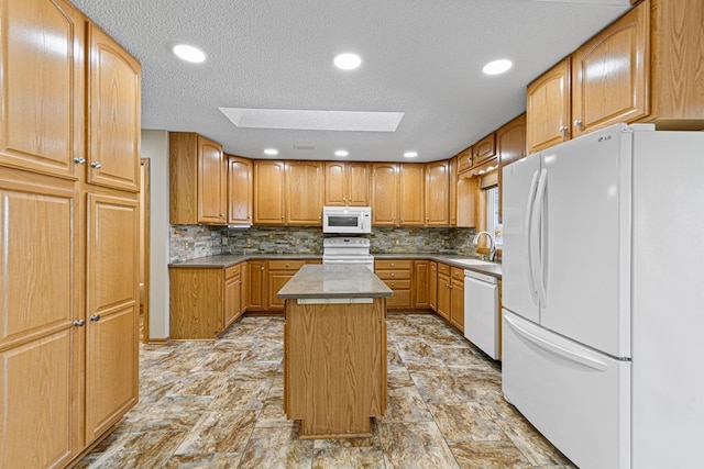 kitchen featuring a textured ceiling, a sink, a kitchen island, white appliances, and a skylight
