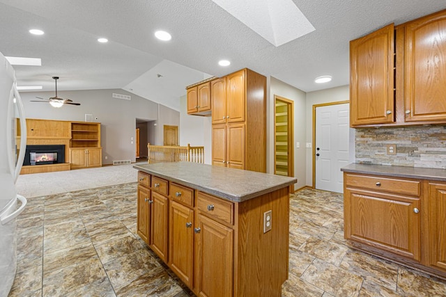 kitchen featuring white fridge, vaulted ceiling with skylight, ceiling fan, a kitchen island, and a glass covered fireplace