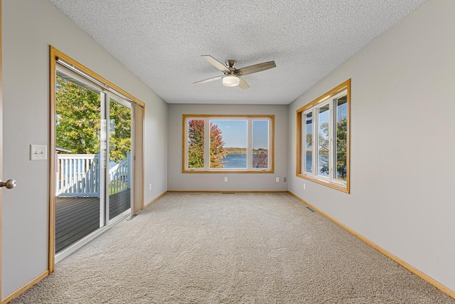carpeted empty room featuring a textured ceiling, ceiling fan, a water view, and baseboards