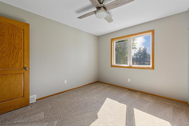 carpeted spare room featuring a textured ceiling, visible vents, a ceiling fan, and baseboards