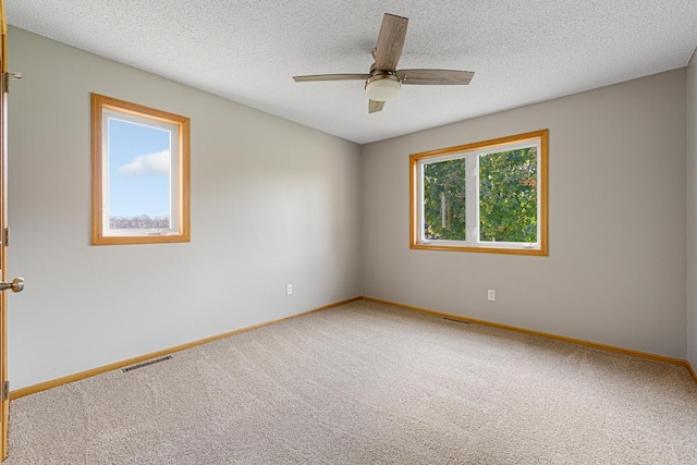 carpeted spare room with a textured ceiling, visible vents, a ceiling fan, and baseboards