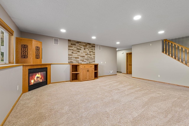 unfurnished living room with recessed lighting, visible vents, light carpet, and a glass covered fireplace
