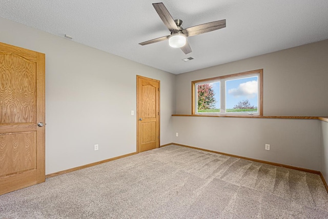 empty room featuring carpet floors, ceiling fan, baseboards, visible vents, and a textured ceiling