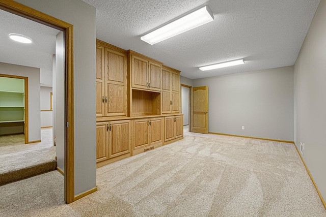 unfurnished living room featuring baseboards, a textured ceiling, and light colored carpet